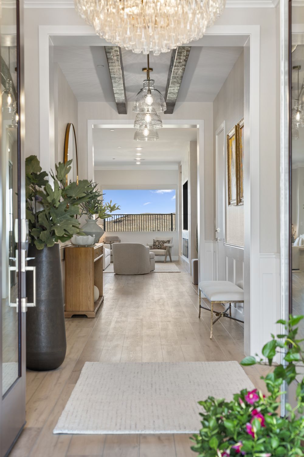 Light-filled entry hall with a crystal chandelier, glass pendants under wood beams, an oak console, and a view through to the living room and desert hills