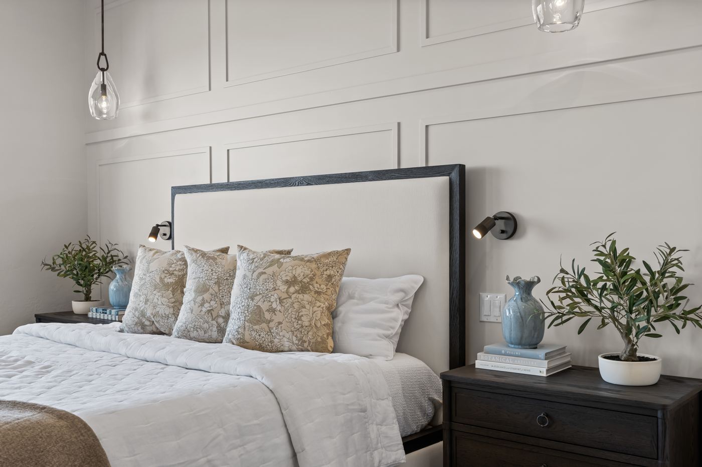 Guest-ready bedroom with an upholstered headboard, floral pillows, and olive trees on the nightstands