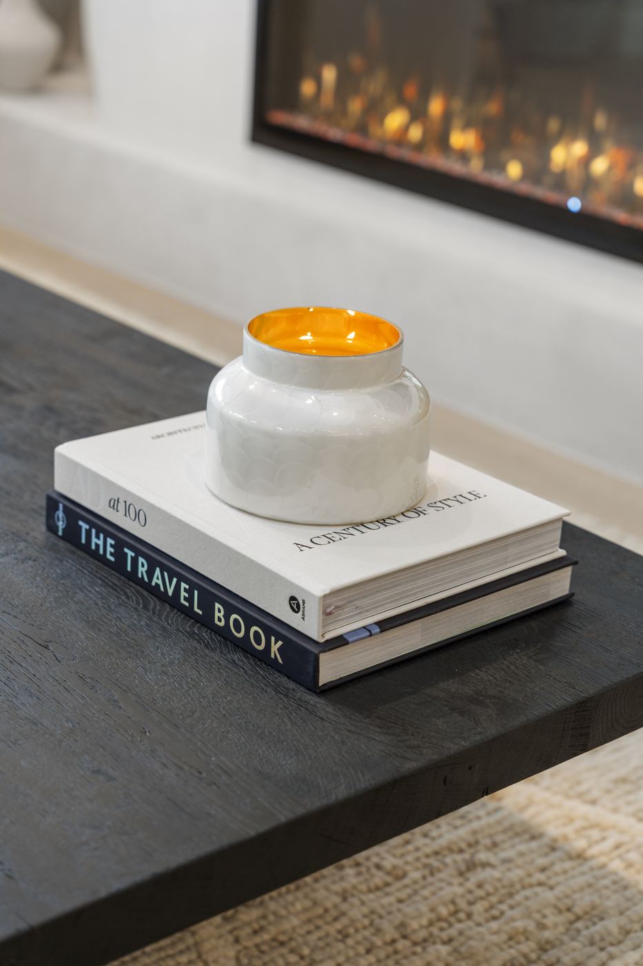 Candle on stacked books atop a dark oak coffee table in front of the fireplace