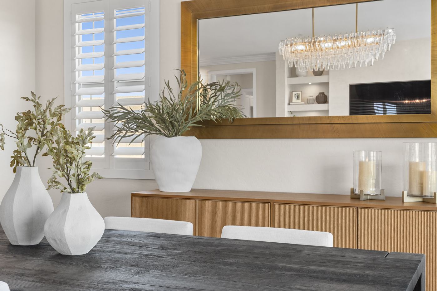 Dining room vignette with white sculptural vases on a dark wood table, a fluted oak sideboard, and a large brass mirror