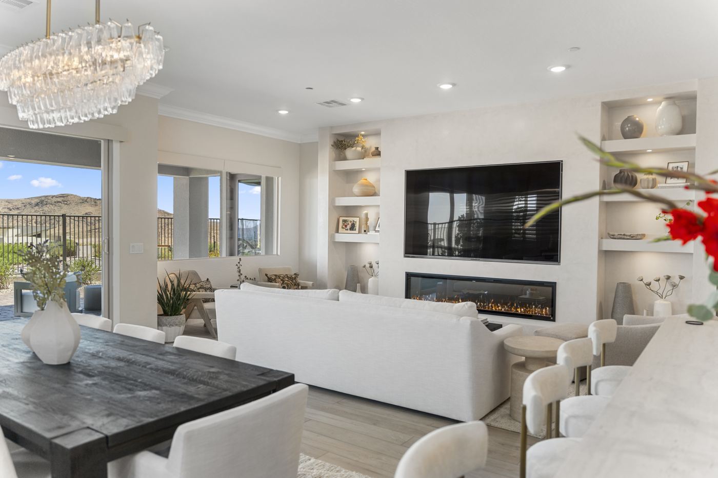 Open great room with a white sofa, dark dining table, crystal chandelier, and lit plaster niches around the fireplace