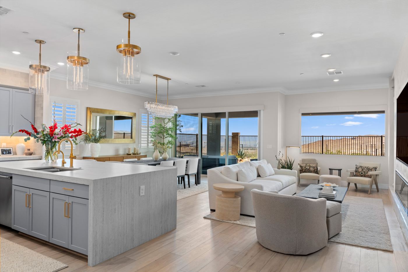Open kitchen and great room with a gray waterfall island, brass pendants, a crystal chandelier over the dining table, and desert views
