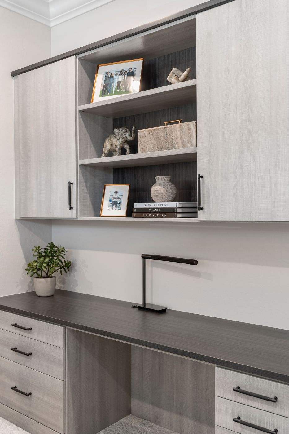 Styled office shelves with framed family photos, a stone box, and a textured vase above a built-in desk