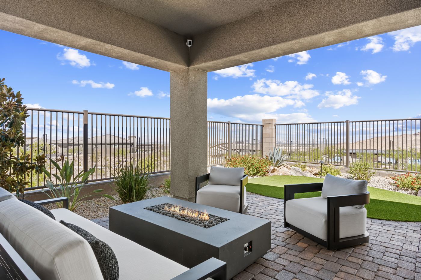 Covered patio with a concrete fire table and white outdoor lounge chairs facing the desert