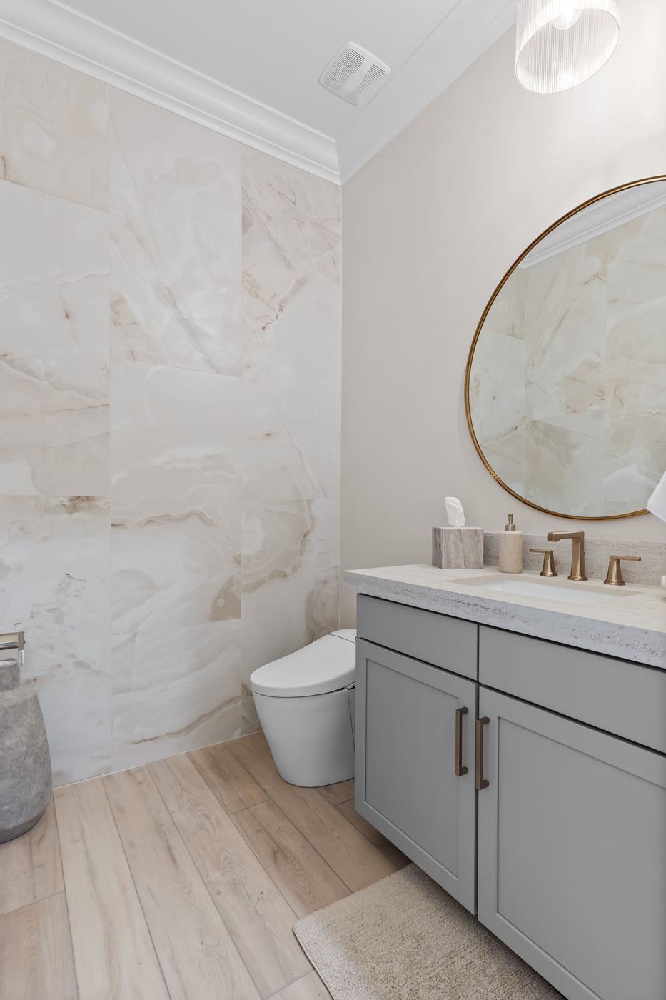 Powder bath with an onyx-look tile wall, round brass mirror, and brushed brass faucet