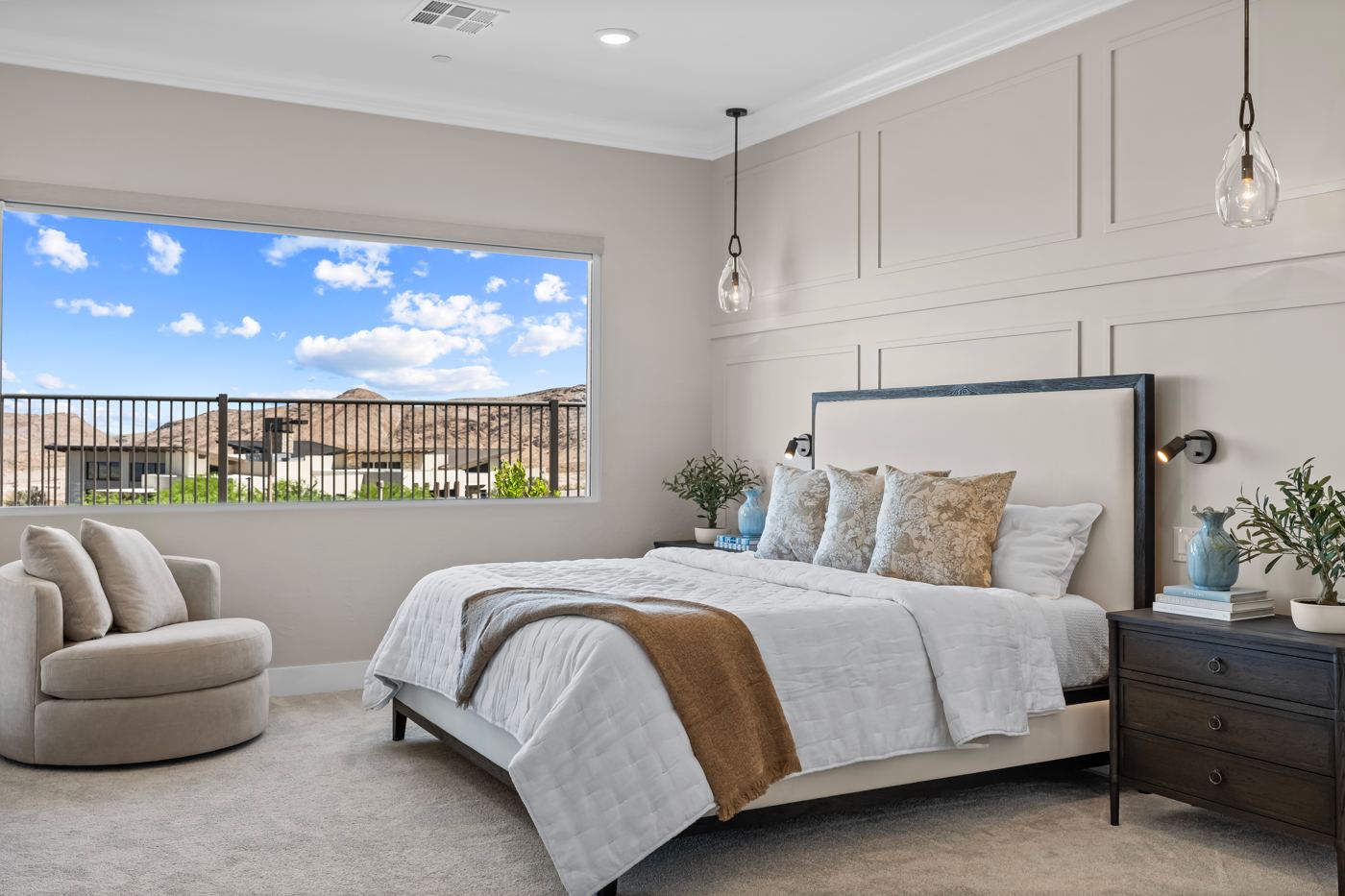 Primary bedroom with a paneled accent wall, upholstered bed, glass pendants, and a picture window onto the hills