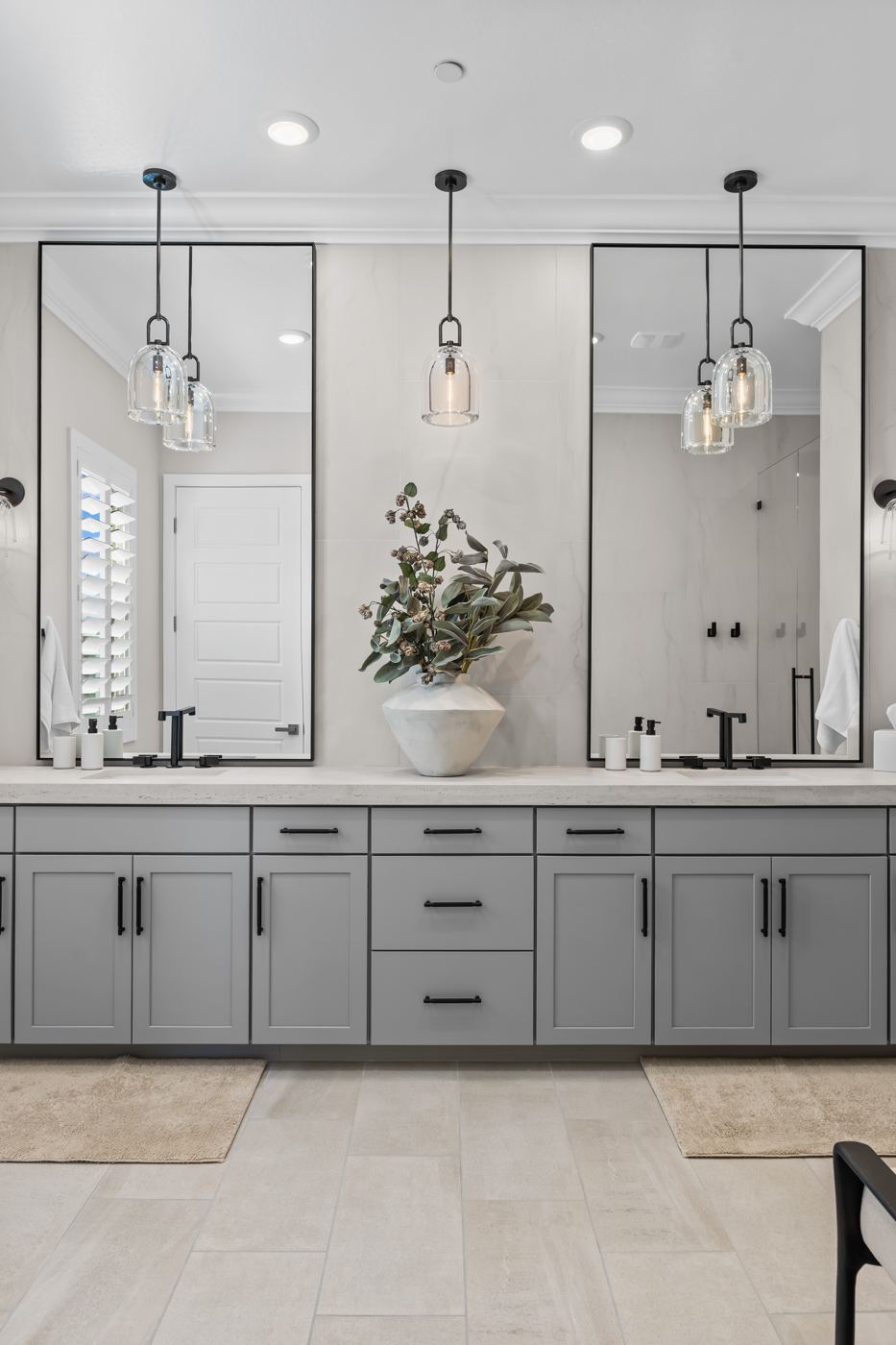 Double vanity in soft gray with tall black-framed mirrors and clear glass pendants