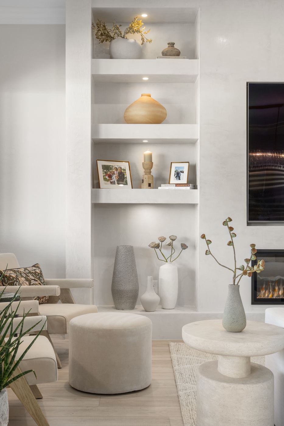 Plaster niche shelves styled with pottery, framed photos, and dried stems above a velvet ottoman