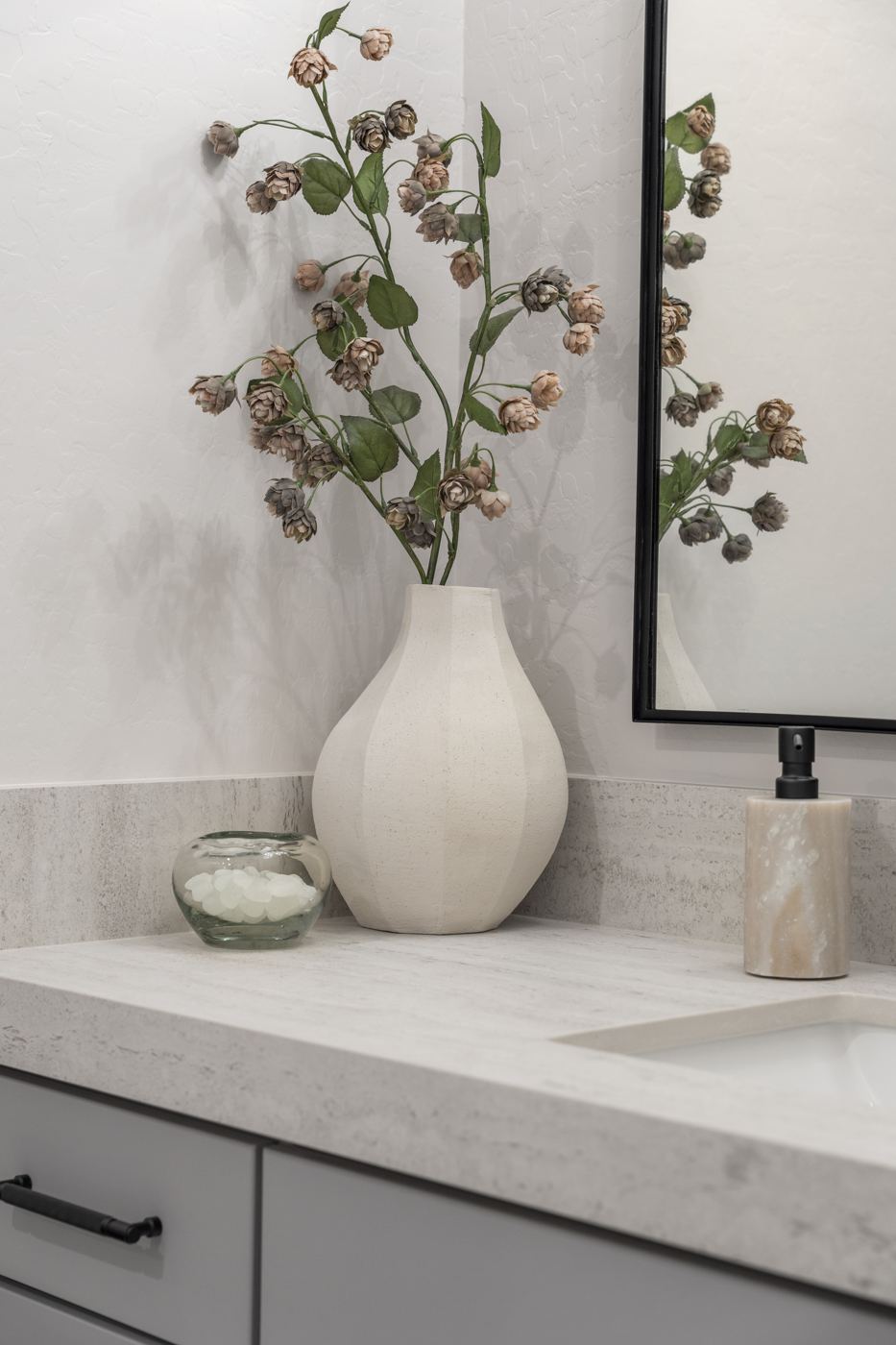 Sculptural white vase with blush stems on a stone vanity top